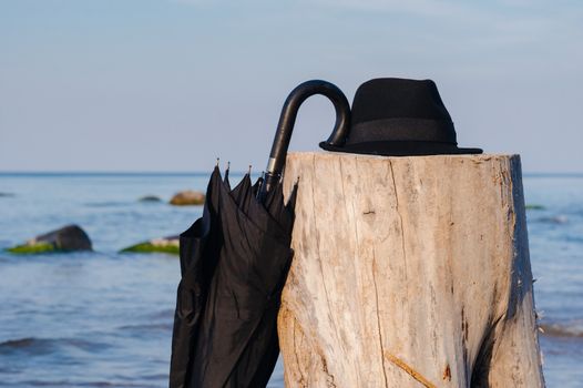 Black umbrella and hat on the wooden stump at the seashore