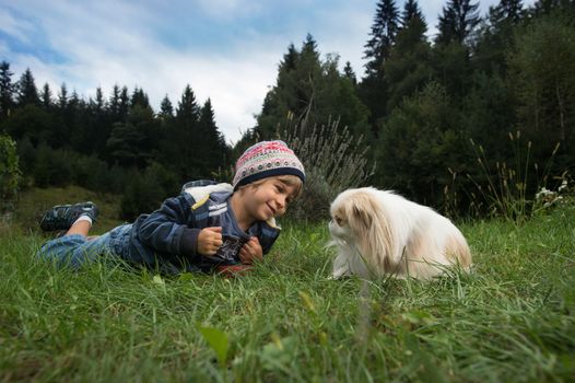 Cute little boy and his dog rolling on the grass looking at each other