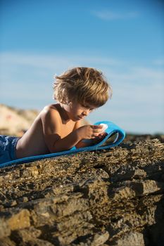 Cute little boy lying on the beach playing with his smart phone. Modern lifestyle, modern generation concept.