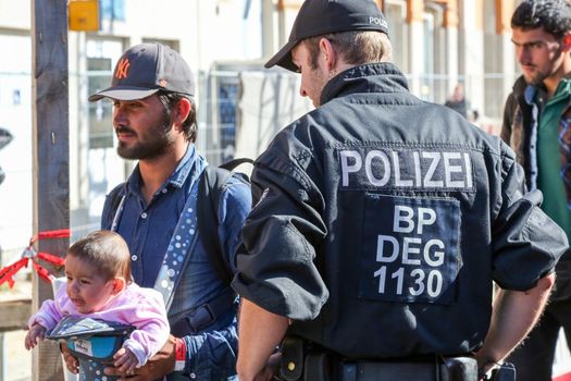 GERMANY, Passau: Security officials stand guard as refugees wait in long queues in the border town of Passau, Germany on September 21, 2015 amid the reintroduction of border controls in Germany, Austria, and a number of other EU countries, aimed at slowing the flow of refugees from war-torn Syria.