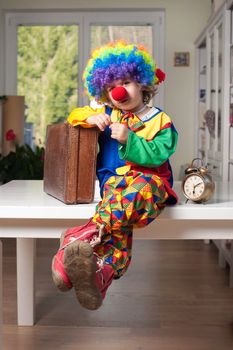 Cute little boy dressed as a clown with a suitcase and clock