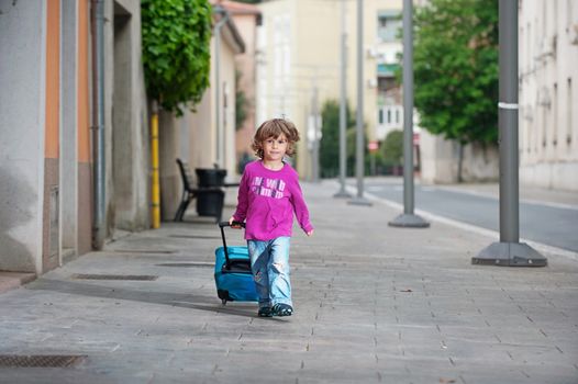 Cute little boy with a luggage bag on the street. Growing up and becoming independent concept.
