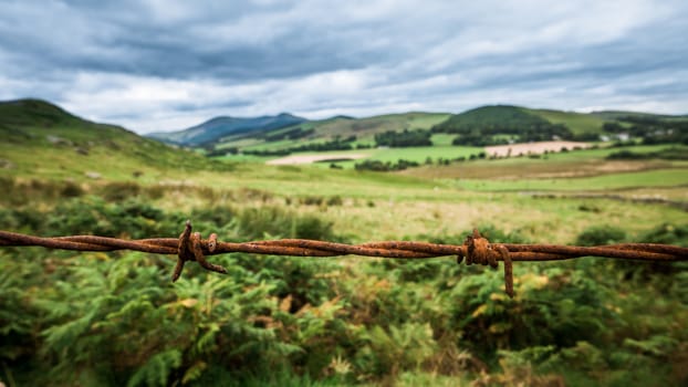 Scenic Landscape Of Rural Countryside With Rusty Barbed Wire In Foreground