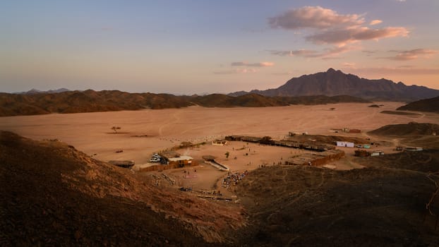 In the picture a beautiful view of a valley in the Egyptian desert at sunset a few kilometers from Marsa Alam, foreground a Bedouin village frequented by many tourists and background the rock mountains.