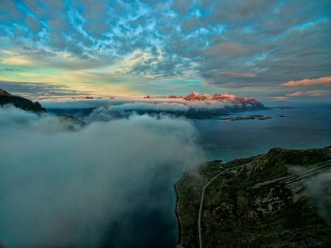 Aerial view above clouds on Lofoten islands with distant peaks lit by midnight sun