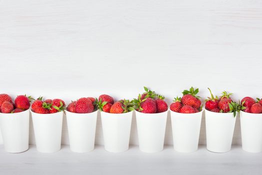 a series of white paper cups with fresh ripe delicious sweet strawberries on a white background