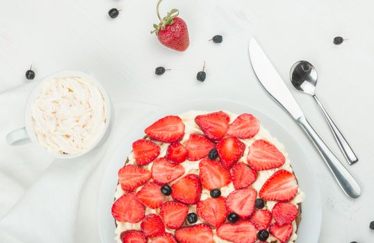 Delicious nutritious cake with fresh strawberries decorated with chokeberry, white cup with whipped cream, steel spoon, strawberry, napkin, knife,  plate, top view,  good morning