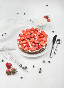 Delicious nutritious cake with fresh strawberries decorated with chokeberry, white cup with whipped cream, steel spoon, whisk, strawberry, napkin, plate, top view,  good morning