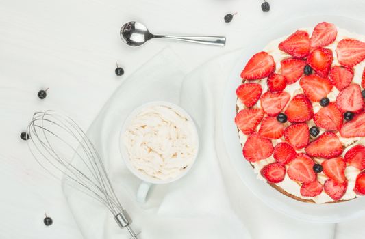 Delicious nutritious cake with fresh strawberries decorated with chokeberry, white cup with whipped cream, steel spoon, strawberry, napkin, knife,  plate, top view,  good morning