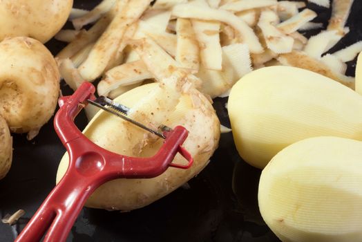 Vegetable peeler, raw potatoes and potato peels on black background, cooking potatoes