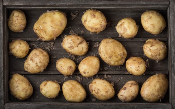Raw new potatoes in an old wooden box as background, top view. Harvest.