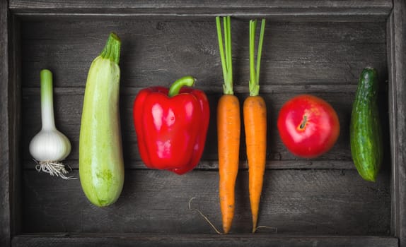 Food for raw foodists. Set of different fresh raw vegetables in an old wooden box: garlic, zucchini, bell pepper, tomato, carrot, cucumber. Harvest. Top view close up.