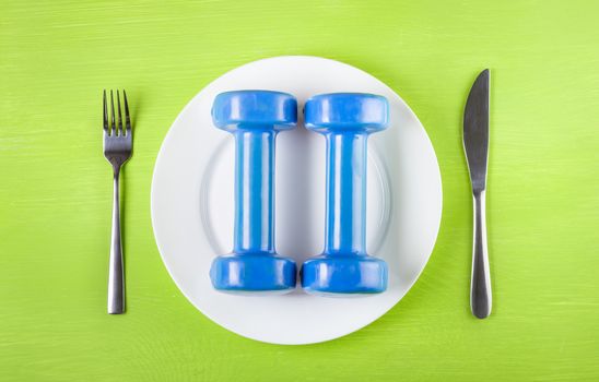 The concept of a healthy lifestyle, diet, sports, weight loss, healthy diet. Dumbbells on a plate, knife, fork, top view, closeup