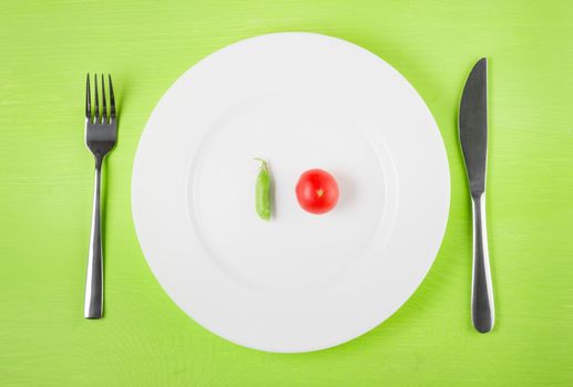 the concept of dietary restrictions, healthy lifestyle, diet,  weight loss, anti-obesity, healthy diet. Small tomato, green peas, on a plate, knife, fork on the table, top view