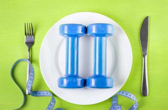 The concept of a healthy lifestyle, diet, sports, weight loss, anti obesity, exercise, healthy diet.  Dumbbells on a plate, centimeter,  knife and fork on the table, top view, closeup