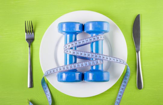 The concept of a healthy lifestyle, diet, sports, weight loss, anti obesity, exercise, healthy diet.  Centimeter and  dumbbells on a plate, knife and fork, on the table, top view, closeup