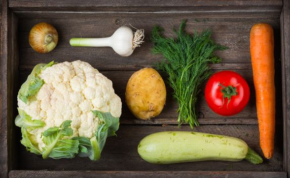 Food for raw foodists. Set of different fresh raw vegetables in an old wooden box: garlic, zucchini, tomato, carrot,  potatoes, cauliflower, onions, dill. Harvest. Ingredients for vegetable dishes