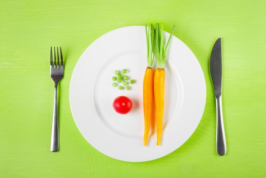 the concept of dietary restrictions, healthy lifestyle, diet,  weight loss, anti-obesity, healthy diet. Small tomato, green peas, two fresh carrots on a plate, knife, fork on the table, top view