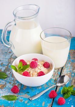Oat flakes with milk and raspberries for breakfast, glass with milk, spoon,  fresh mint on an old wooden blue background, the concept of a healthy diet, weight loss