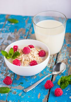 Oat flakes with milk and raspberries for breakfast, glass with milk, spoon,  fresh mint on an old wooden blue background, the concept of a healthy diet, weight loss