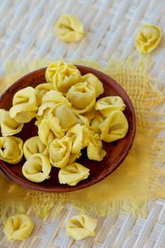 Raw Meat Cappelletti on Brown Plate with Yellow Napkin closeup on Wicker background