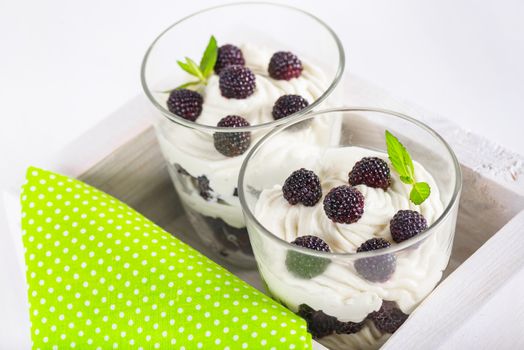 delicious soft cheese dessert with whipped cream and fresh blackberries with a sprig of fresh mint in a glass, in a decorative wooden box on a white table