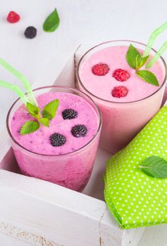 Raspberry and blackberry dairy smoothies with fresh berries and sprigs of mint in a decorative white box on a white wooden table