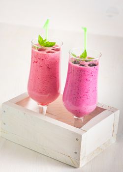 Raspberry and blackberry dairy smoothies with fresh berries and sprigs of mint in a decorative white box on a white wooden table