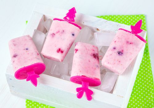 Homemade ice cream, frozen yogurt with blackberries, blueberries and raspberries, white wooden box with ice, bright green napkin in white polka dots print on a white table