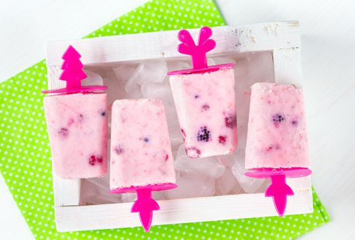 Homemade ice cream, frozen yogurt with blackberries, blueberries and raspberries, white wooden box with ice, bright green napkin in white polka dots print on a white table, top view