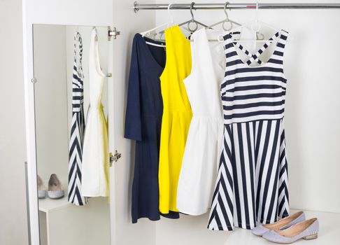 a series of bright modern fashion women's dresses on hangers in a white cupboard for summer and spring