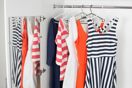 a series of bright modern fashion women's dresses on hangers in a white cupboard for summer and spring