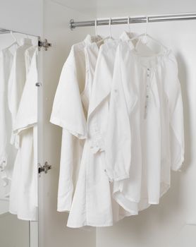 set of white clean ironed clothes hanging on hangers in a white cabinet