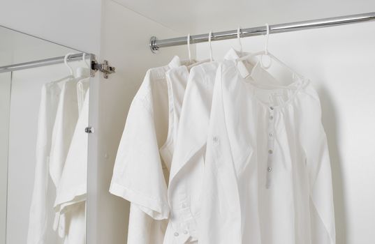 set of white clean ironed clothes hanging on hangers in a white cabinet