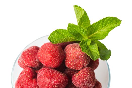 Frozen strawberries in a ice-cream bowl, a sprig of fresh mint top view on a white background