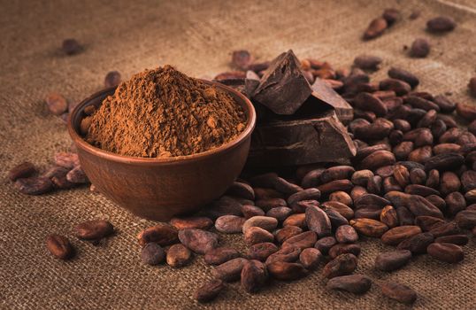 Cocoa beans, clay bowl with cocoa powder, chocolate on brown sacking