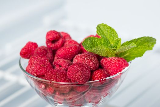 frozen raspberries in a glass piala in the freezer and a sprig fresh of mint