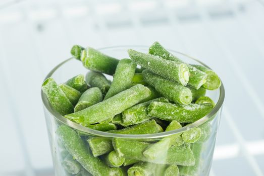 Frozen green cow-pea pods in a glass in the freezer, close up 