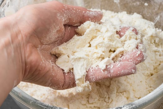 a hand mixing the flour and butter in a glass bowl for baking