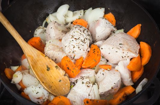 Cooking turkey with vegetables and spices in a frying pan fried minced raw turkey into pieces, chopped carrots, onions and dried herbs, wooden spoon mixing meat