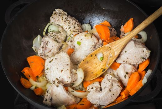 Cooking turkey with vegetables and spices in a frying pan fried minced raw turkey into pieces, chopped carrots, onions and dried herbs, wooden spoon mixing meat