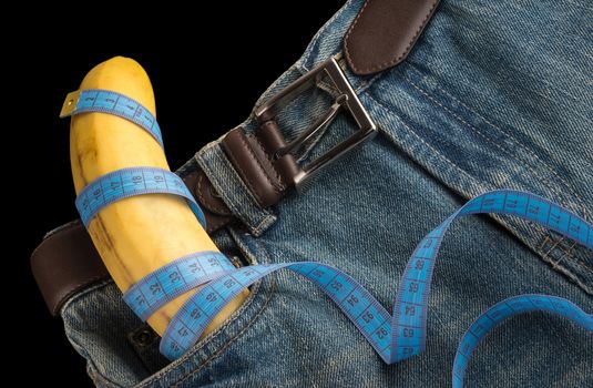 Big Banana like the penis, men's jeans, belt and centimeter, top view, on dark background