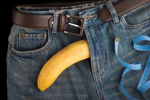 Big Banana like the penis, men's jeans, belt and centimeter, top view, on dark background