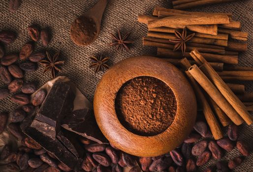 Raw cocoa beans, raw dark  homemade chocolate for raw foodists, cinnamon sticks, star anise and cocoa powder in a wooden bowl, top view