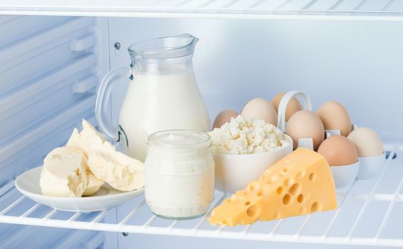 eggs and tasty healthy dairy products in the refrigerator: sour cream in the bank, cottage cheese in  bowl, eggs, cheese, butter on a saucer and milk in a jar