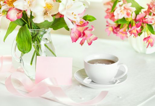Beautiful bouquet of alstroemeria in a vase with water,  white cup of tea, greeting card with the inscription mother's day, pink ribbon on the table at home in the kitchen, love concept