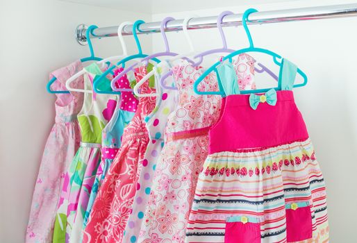 row of bright colorful little girl dresses hanging on coat hanger in white wardrobe