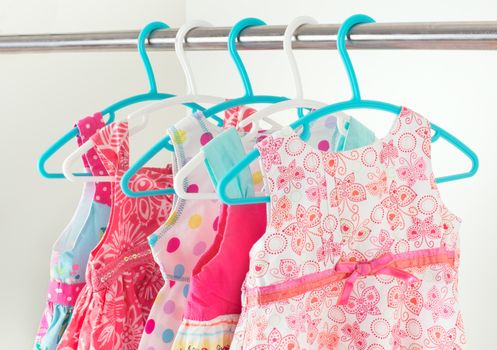 row of bright colorful little girl dresses hanging on coat hanger in white wardrobe