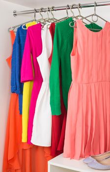 bright colorful female dresses and sweaters  hanging on coat hanger,  shoes and handbag in white wardrobe