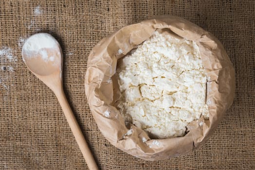 Whole flour in a paper bag and a wooden spoon on sacking, close up, top view